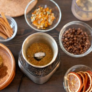 Group of bowls with coffee beans, dry flowers and orange slices, cinnamon sticks, ground candied fruits and other ingredients for making soap