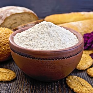 Amaranth flour in a clay bowl with bread and biscuits, purple amaranth flower on the background of wooden boards