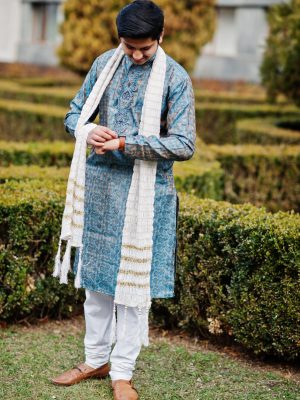 Indian man wear on traditional clothes with white scarf posed outdoor against green bushes at park, looking at his watches.